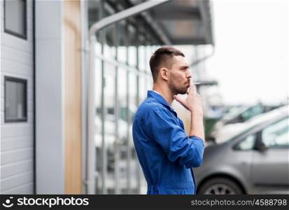 service, repair, maintenance and people concept - auto mechanic smoking cigarette at car shop or garage outdoors