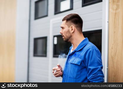 service, repair, maintenance and people concept - auto mechanic smoking cigarette at car shop or garage outdoors