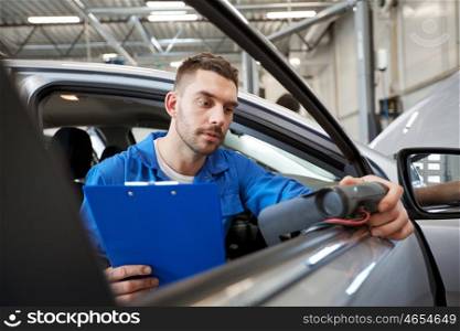 service, repair, maintenance and people concept - mechanic man with automotive diagnostic scanner and clipboard checking car system at workshop