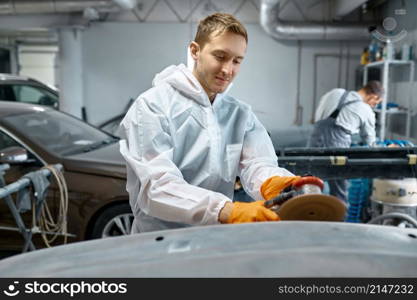 Serviceman polishing car body part with grinding machine in workshop. Garage painting auto service. Serviceman polishing car body part in workshop