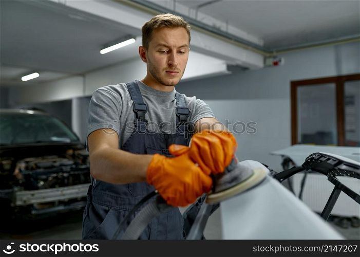 Serviceman polishing car body part with grinding machine in workshop. Garage painting auto service shop. Serviceman polishing car body part in workshop
