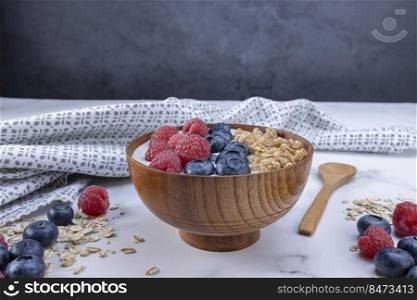 Serving a portion of yogurt with blueberry raspberry and oat flakes in a wooden bowl ready to be served. Healthy food for dieting concept. Fruit muesli with yogurt.