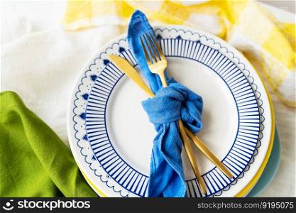 Serving design. Easter serving concept. Gold cutlery is tied with a blue napkin, on which the plates are on a green-yellow linen napkin. Minimalistic design. Serving design. Easter serving concept. Gold cutlery is tied with a blue napkin, on which the plates are on a green-yellow linen napkin. Minimalistic design.