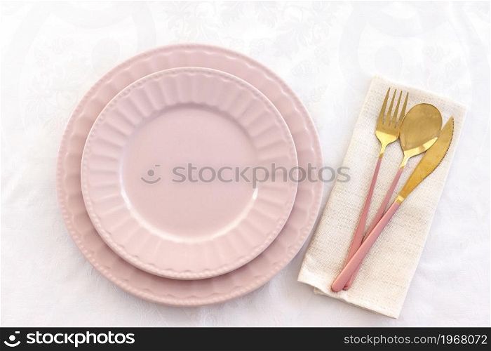 serving. two pink plates on a white tablecloth and a pink-gold fork, knife, and spoon on a linen napkin.