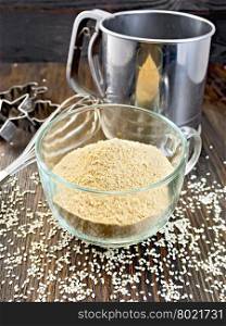 Sesame flour in a glass cup with strainer and mixer, sesame seeds on a wooden boards background