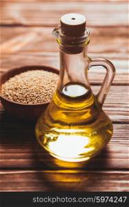 Sesame oil in a glass bottle with a cork and heap sesame seeds in a wooden bowl. The sesame oil