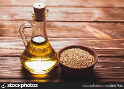 Sesame oil in a glass bottle with a cork and heap sesame seeds in a wooden bowl. The Sesame oil