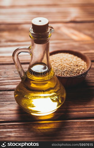 Sesame oil in a glass bottle with a cork and heap sesame seeds in a wooden bowl. The Sesame oil