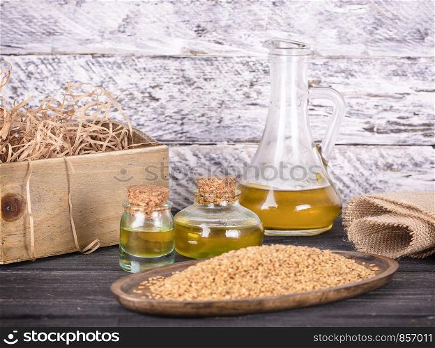 Sesame oil in glass and seeds on lod wooden background