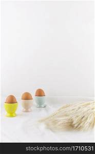 set easter eggs cups near bunch wheat light textile