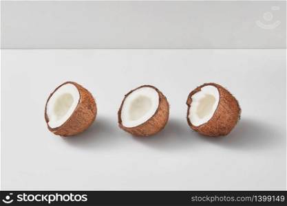 Set from three fresh ripe natural organic coconut halves on a duotone light grey background with soft shadows, copy space. Vegan concept.. Three halves of fresh ripe organic coconut on a light grey background.