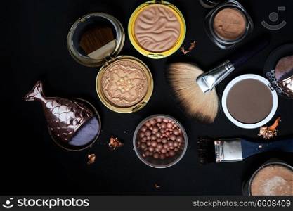 Set of bronze powder with makeup brushes on black background