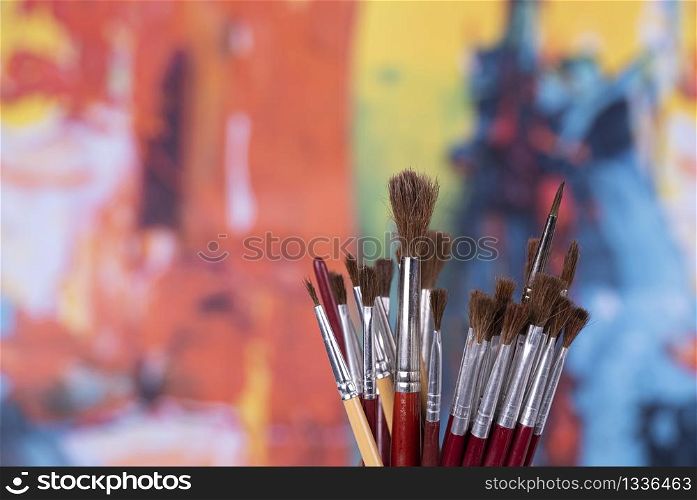 set of brushes in a jar in front of an abstract coloured background