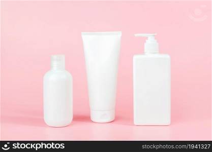 Set of care cosmetic for skin, body or hair. Three white blank cosmetics bottles, tube on pink background. Spa Cosmetic Beauty Concept. Front view Mockup.. Set of care cosmetic for skin, body or hair. Three white blank cosmetics bottles, tube on pink background. Spa Cosmetic Beauty Concept. Front view Mockup
