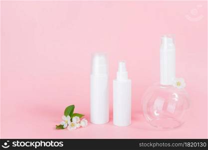 Set of cosmetic for skin care face, body. White blank cosmetics bottles and tube on glass podium and flowering branch, pink background. Natural Organic Spa Cosmetic Beauty Concept Mockup.. Set of cosmetic for skin care face, body. White blank cosmetics bottles and tube on glass podium and flowering branch, pink background. Natural Organic Spa Cosmetic Beauty Concept Mockup
