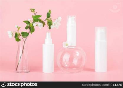 Set of cosmetic for skin care face, body. White blank cosmetics bottles and tube on glass podium and flowering branch in vase, pink background. Natural Organic Spa Cosmetic Beauty Concept Mockup.. Set of cosmetic for skin care face, body. White blank cosmetics bottles and tube on glass podium and flowering branch in vase, pink background. Natural Organic Spa Cosmetic Beauty Concept Mockup