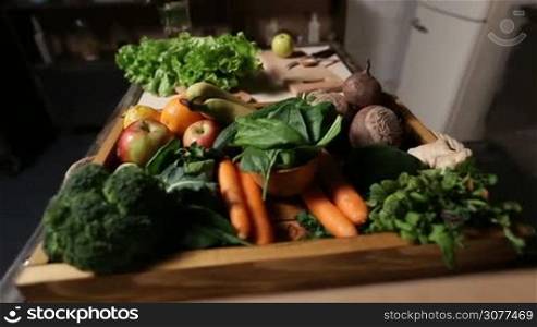 Set of different green fresh raw vegetables and fruits in the wooden tray for cooking healthy food closeup. Green salad, cutting board, knife and spoon on background. Fresh raw organic ingredients for preparation of vegetarian smoothie.