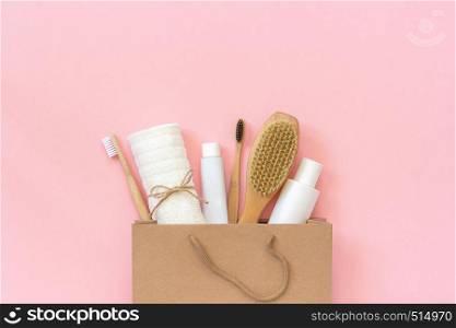 Set of eco cosmetics products and tools for shower or bath Bamboo toothbrush, natural brush, white bottles, towel accessories for body, face and teeth care in paper bag on pink background Copy space. Set of eco cosmetics products and tools for shower or bath Bamboo toothbrush, natural brush, white bottles, towel accessories for body, face and teeth care in paper bag on pink background. Copy space
