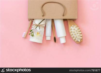 Set of eco cosmetics products and tools for shower or bath Bamboo toothbrush, natural brush, white bottles, towel accessories for body, face and teeth care in paper bag on pink background Copy space. Set of eco cosmetics products and tools for shower or bath Bamboo toothbrush, natural brush, white bottles, towel accessories for body, face and teeth care in paper bag on pink background. Copy space