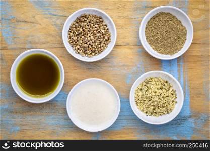 set of hemp seed product:s hearts, protein powder, milk and oil in small white bowls against grunge wood