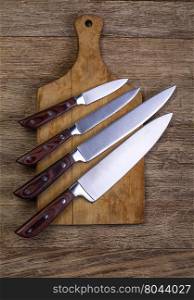 Set of kitchen knifes on wooden cutting board on old wooden table