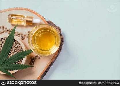 Set of legalized marijuana includes green hemp leaf, CBD oil in a bottle with a dropper lid and a glass bowl, and hemp seed displayed on a wooden plate.. Set of legalized marijuana products displayed on a wooden plate.