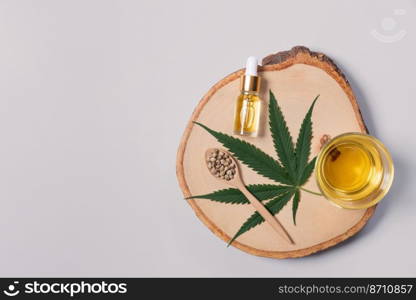 Set of legalized marijuana includes green hemp leaf, CBD oil in a bottle with a dropper lid and a glass bowl, and hemp seed displayed on a wooden plate.. Set of legalized marijuana products displayed on a wooden plate.