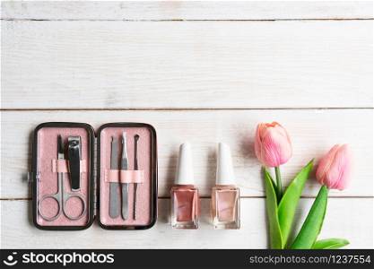 Set of manicure instruments and tools in pink case with nail polish on white wooden background, top view, copy space