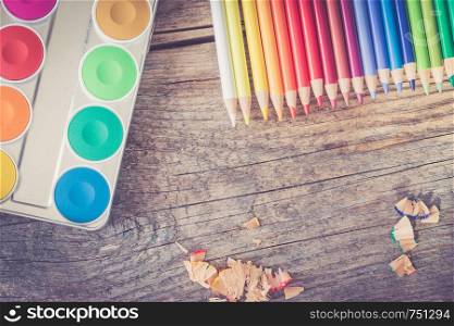 Set of multi-colored pencils, water colors and brushes on a rustically wooden table, copy space