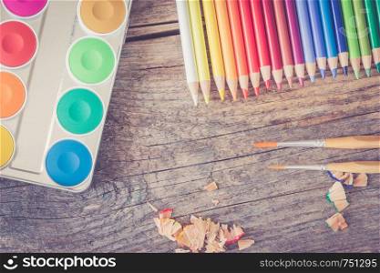 Set of multi-colored pencils, water colors and brushes on a rustically wooden table, copy space