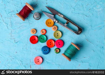 Set of pied buttons for garment with threads on blue background. Colorful plastic buttons