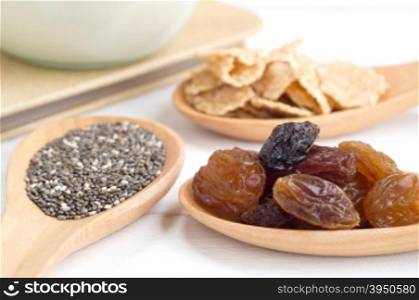 Set of raisins, whole wheat grain flakes and chia seeds in wooden spoon and milk on white wood background with selective focus point&#xA;