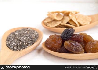 Set of raisins, whole wheat grain flakes and chia seeds in wooden spoon on white wood background&#xA;with selective focus point.