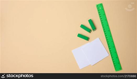 set of stationery objects ruler, blank white paper sheets ina beige background. View from above