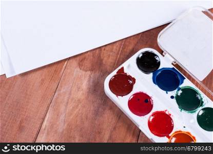 Set of watercolor paints in white base, sheets of white watercolor paper,brush on light wooden background