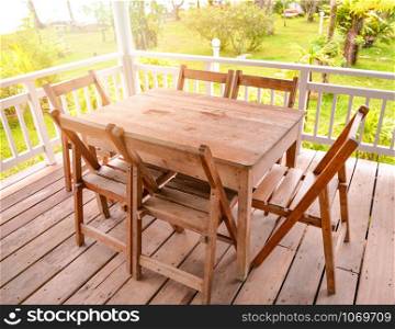 Set of wooden table dining and chairs on balcony terrace with front yard green grass and summer garden background