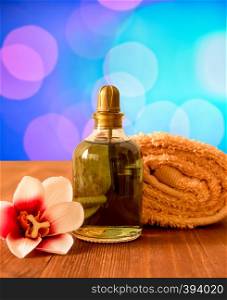 Set on for spa and wellness. Rolled towel, bottle of oil and orchid flower on a wooden background.. Towel, bottle with oil and orchid flower on wooden background