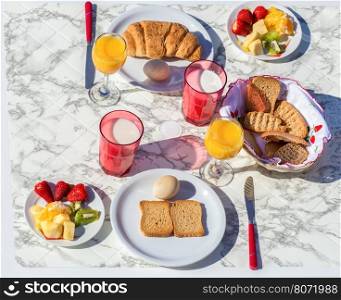 Set table with various food and drink for breakfast on sunny day in summer season