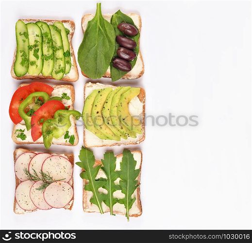 Set with toast bread and different vegan toppings on white background, top view. Toasts with avocado, spinach, arugula and other vegetables ingridients. Healthy snack or vegan food concept. Copy space.. Set with toast bread and different vegan toppings on white background, top view. Toasts with avocado, spinach, arugula and other vegetables ingridients. Healthy snack or vegan food concept