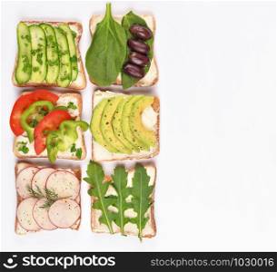 Set with toast bread and different vegan toppings on white background, top view. Toasts with avocado, spinach, arugula and other vegetables ingridients. Healthy snack or vegan food concept. Copy space.. Set with toast bread and different vegan toppings on white background, top view. Toasts with avocado, spinach, arugula and other vegetables ingridients. Healthy snack or vegan food concept