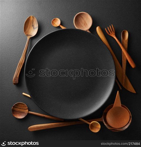setting empty black plate and wooden spoon, fork, knife on a black table.. setting empty plate and wooden cutlery