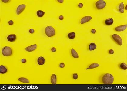 Setting of in shell almonds, chestnuts and hazelnuts on yellow background top view
