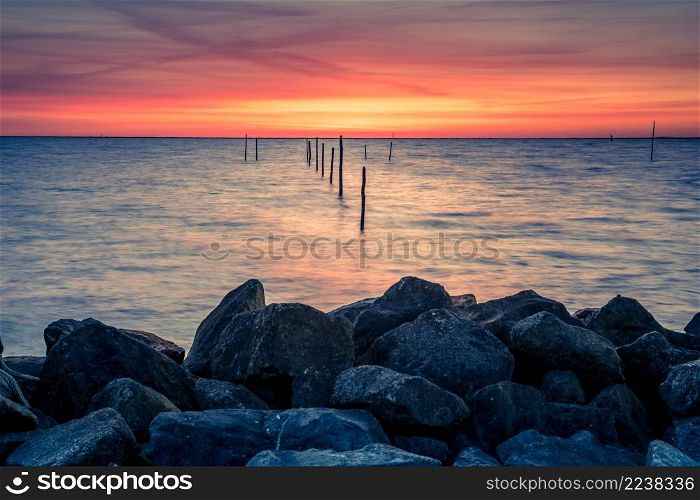 Setting sun above Dutch IJsselmeer with poles of fish trap in foreground, Lake IJssel, Flevoland, Netherlands. Setting sun with fish trap at the coast