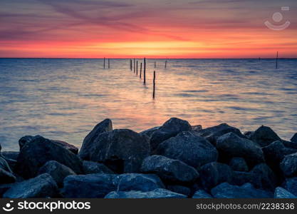 Setting sun above Dutch IJsselmeer with poles of fish trap in foreground, Lake IJssel, Flevoland, Netherlands. Setting sun with fish trap at the coast