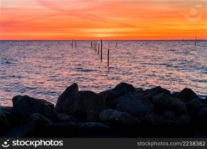 Setting sun above Dutch IJsselmeer with poles of fish trap in foreground, Lake IJssel, Flevoland, Netherlands. Setting sun with fish trap at the coast