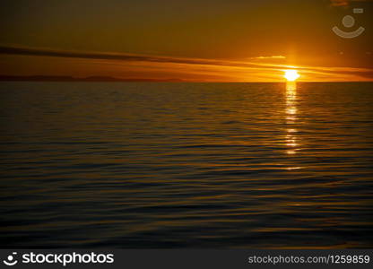 Setting sun colors sky golden in calm sea in Antarctica