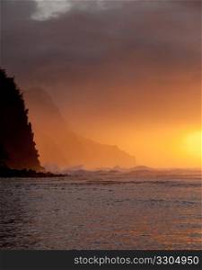 Setting sun illuminates the clouds over Na Pali coast on Kauai with stormy ocean pounding in
