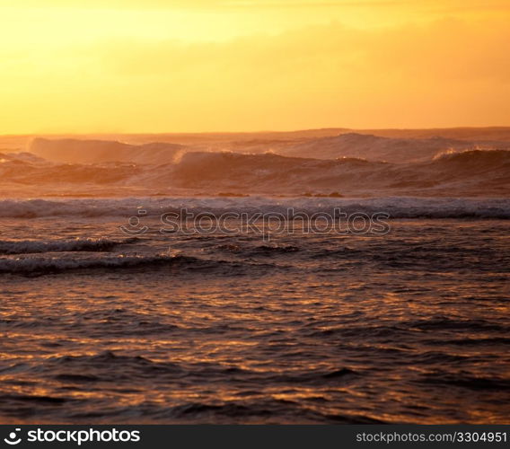 Setting sun illuminates the waves over Na Pali coast on Kauai with stormy ocean pounding in