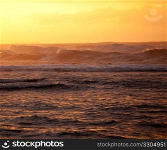 Setting sun illuminates the waves over Na Pali coast on Kauai with stormy ocean pounding in