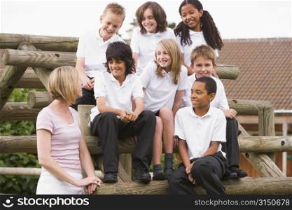 Seven students sitting on wooden structure with teacher standing beside them